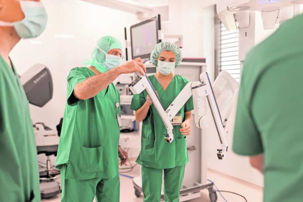 A medical team in green uniforms uses a surgical robotic system in the operating room.