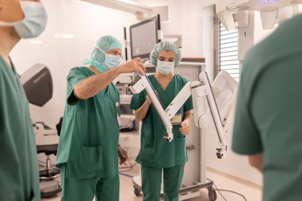 Medicinski tim u zelenim kutama i maskama postavlja robotski kirurški sustav u operacijskoj sali.