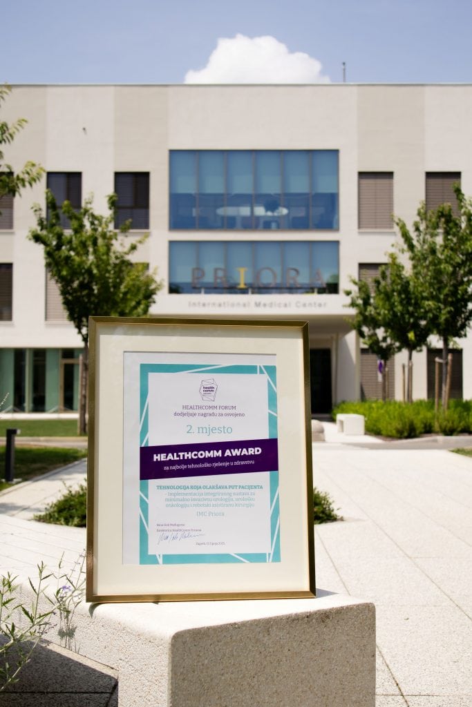 Uokvirena nagrada Healthcomm Forum za drugo mjesto u kategoriji najboljeg tehnološkog rješenja u zdravstvu stoji ispred zgrade s natpisom 'PRIORA International Medical Center'.