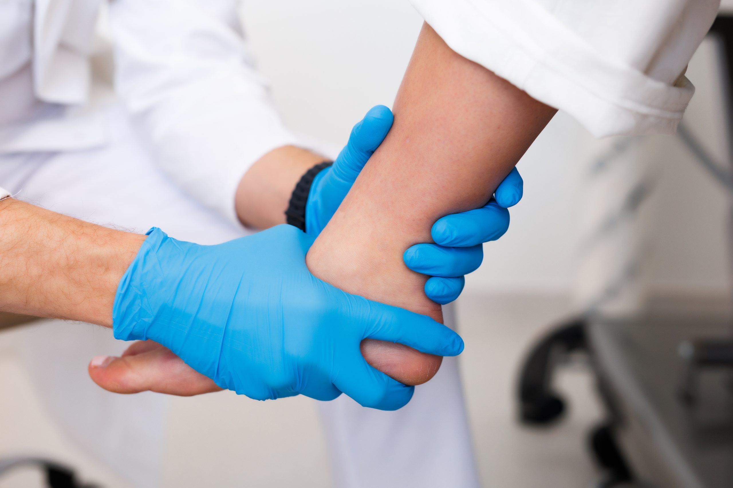 Liječnik u plavim rukavicama pregledava pacijentov zglob gležnja, držeći stopalo i provjeravajući pokretljivost.