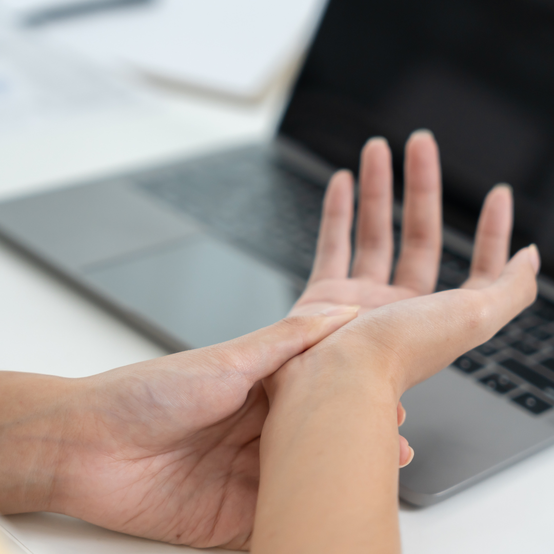 Osoba masira zglob šake ispred otvorenog laptopa.