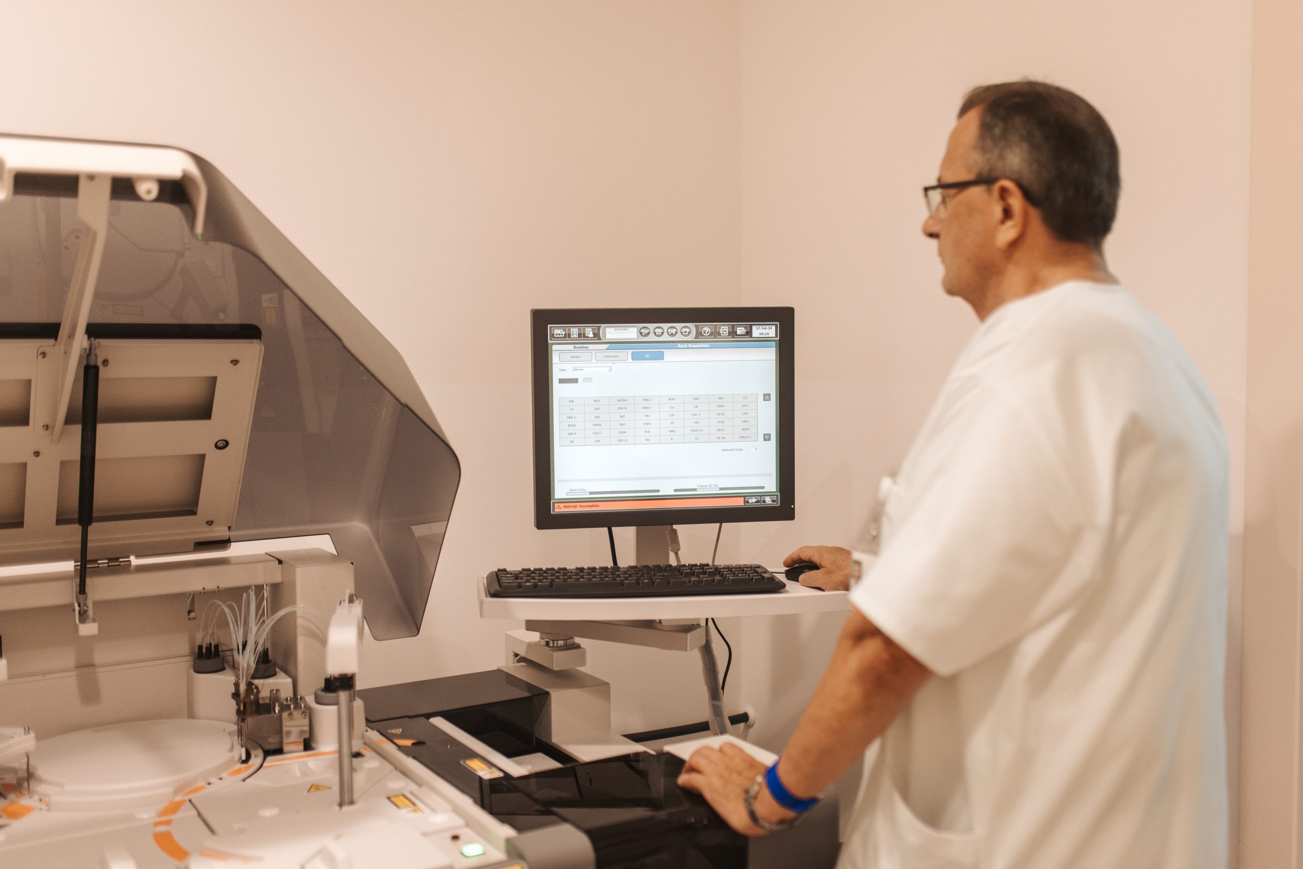 Laboratorijski tehničar u bijeloj kuti radi na analizatoru uz računalni ekran s prikazom rezultata testova.