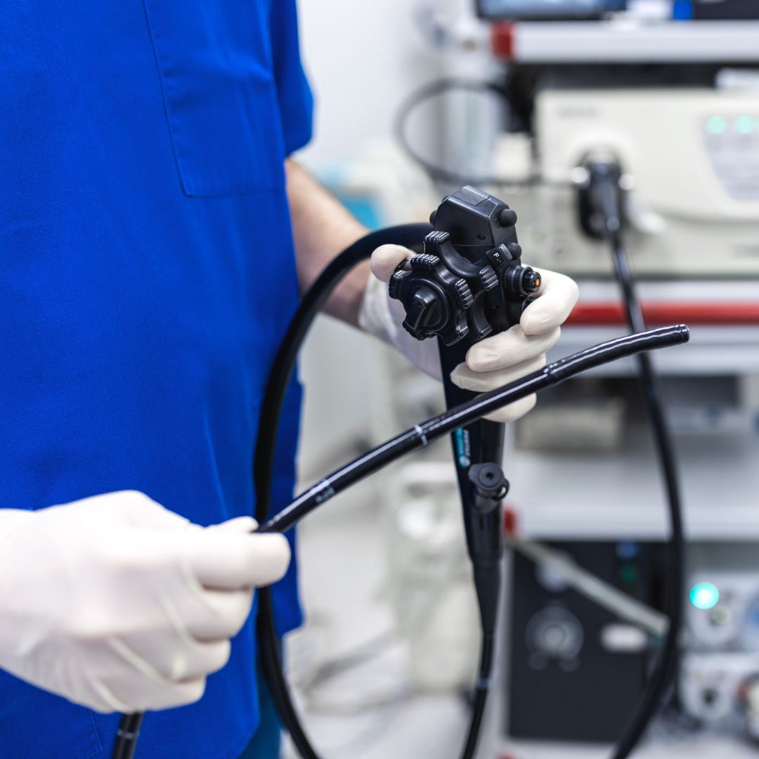 Medicinski tehničar u plavoj uniformi drži endoskop s crijevom u sterilnoj prostoriji za pregled.