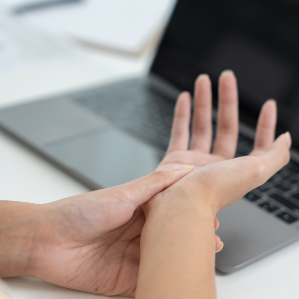 Osoba masira zglob šake ispred otvorenog laptopa.