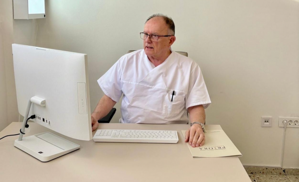 Muškarac u bijeloj medicinskoj uniformi sjedi za računalom u ordinaciji; na stolu mapa s natpisom FELORA.