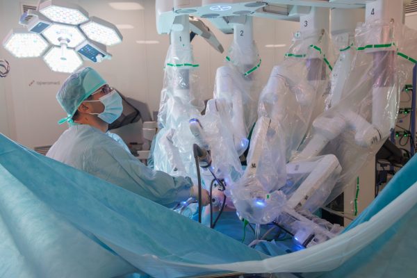 Kirurg upravlja robotskim kirurškim sustavom s više sterilno prekrivenih ruku u operacijskoj sali.