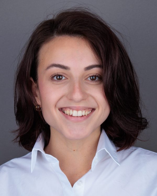 Smiling young woman with short dark hair in a white collared shirt against a gray background