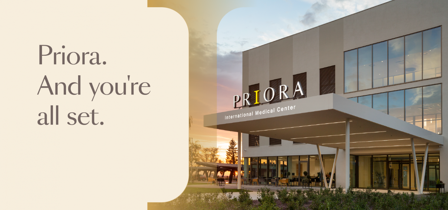 Modern medical center entrance at sunset with sign reading “PRIORA International Medical Center” and tagline “Priora. And you’re all set.”