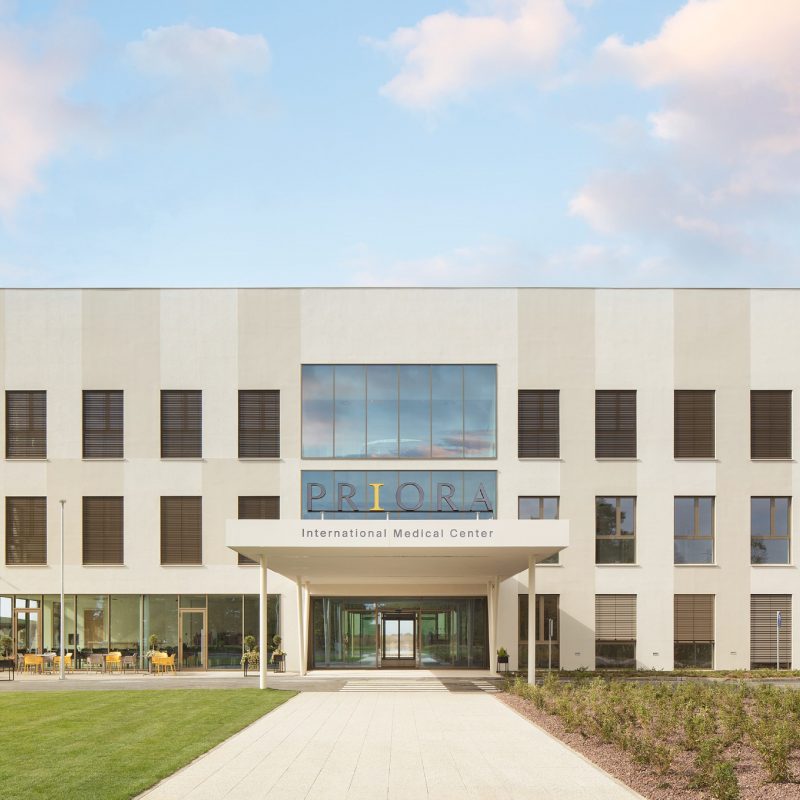Prednja fasada zgrade međunarodnog medicinskog centra PRIO, modernog dizajna s velikim prozorima i natpisom iznad ulaza.