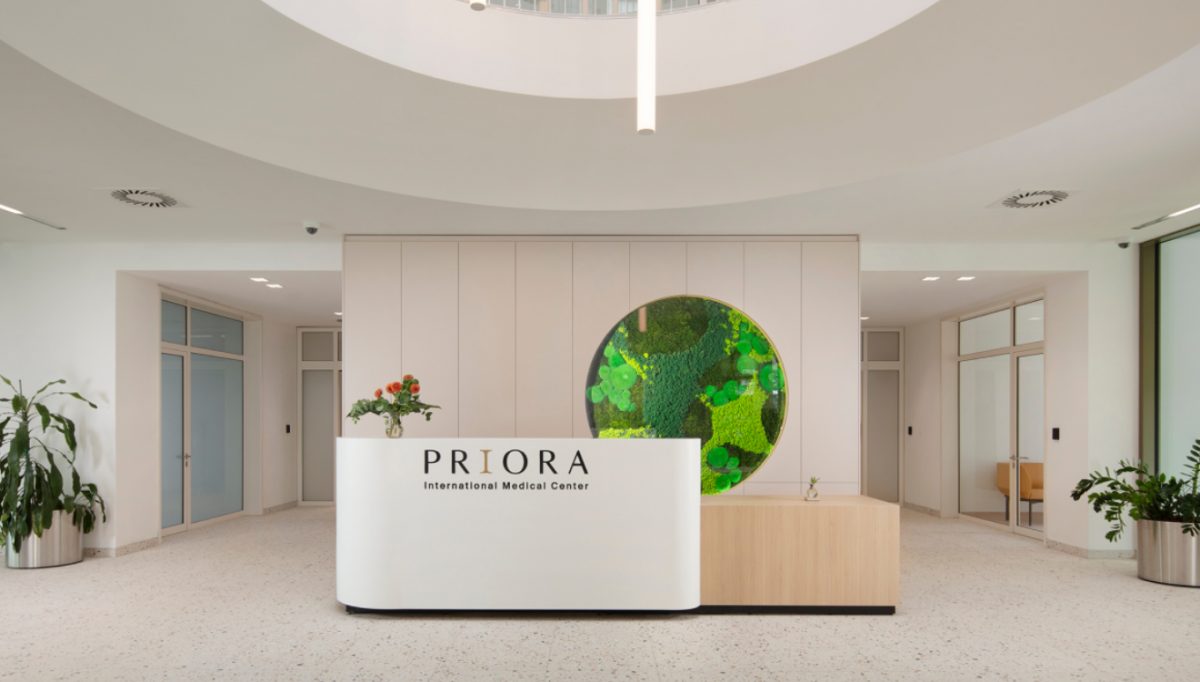 Recepcija medicinskog centra "PRIORA" s modernim dizajnom, okruglim zelenim umjetničkim djelom na zidu i biljkama u loncima.