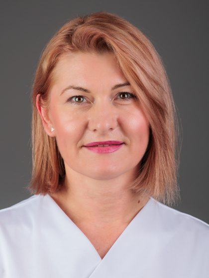 Žena s kratkom smeđom kosom u bijeloj uniformi na sivoplavoj pozadini.