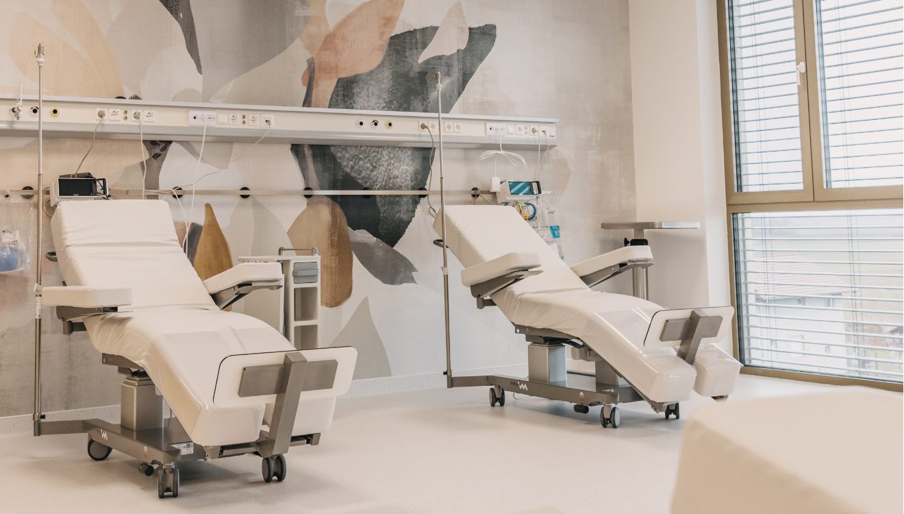 Dvije bijele medicinske stolice u modernoj klinici, s velikim prozorom i apstraktnom umjetnošću na zidu.