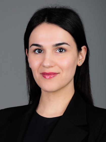 Mlada žena s dugom crnom kosom i svijetlom puti nosi crni sako, s neutralnom pozadinom.