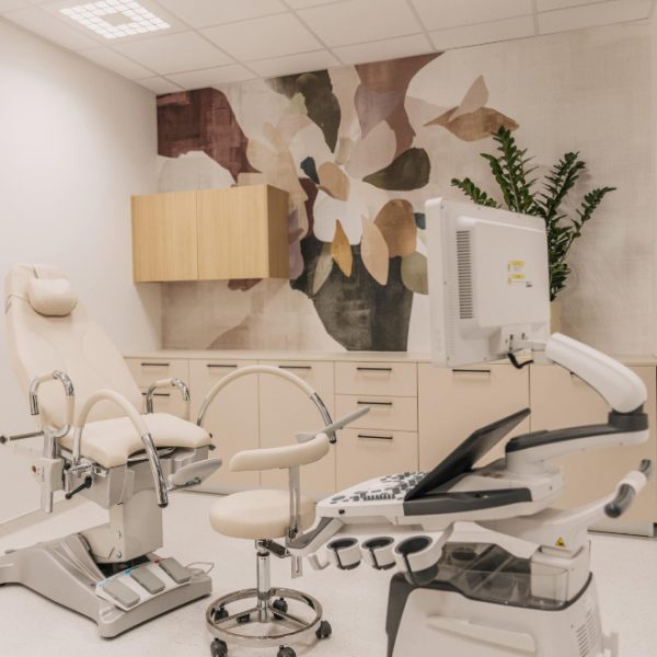 Moderno opremljena ordinacija s medicinskim stolicom, monitorom i medicinskom opremom, ukrašena zidnim umjetničkim djelom s biljnim motivima i biljkama u kutu.