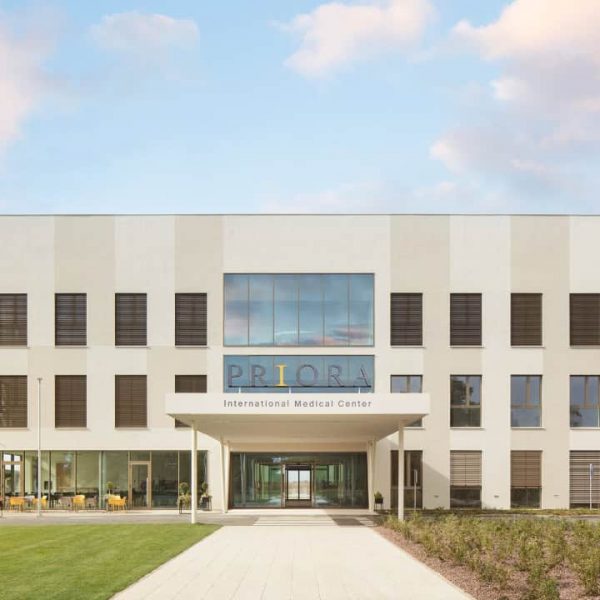 Moderni ulaz u međunarodni medicinski centar PRIORA sa staklenim prozorima i urednim vanjskim prostorom.