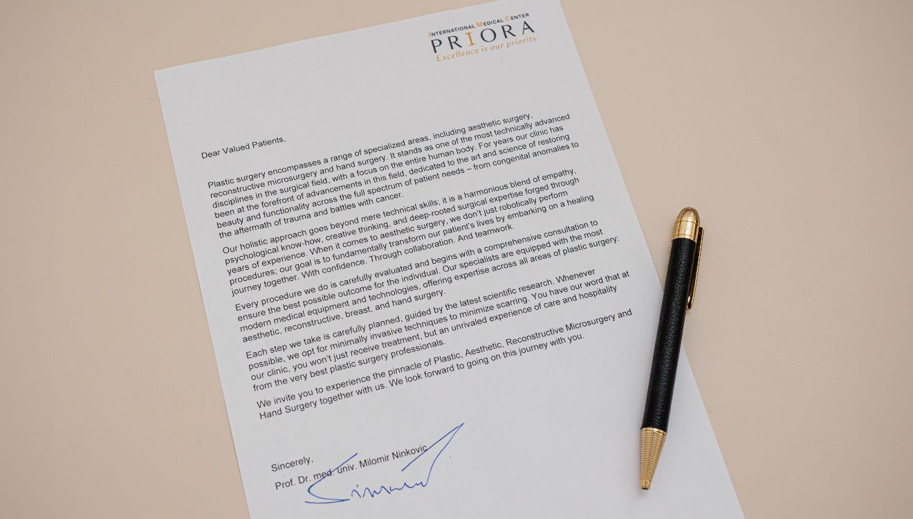 Pismo na službenom papiru centra PRIORA s potpisom ispod, položenim na bež površinu uz crno-zlatnu kemijsku olovku. Sadržaj pisma se obraća pacijentima i govori o plastičnoj kirurgiji i holističkom pristupu liječenju.