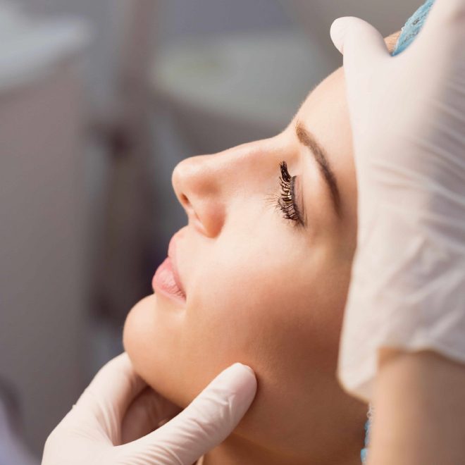 Žena zatvorenih očiju leži na boku dok joj osoba u rukavicama nježno drži lice, vjerojatno tijekom kozmetičkog tretmana.