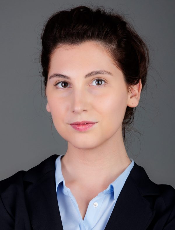 Mlada žena s tamnom kosom u poslovnom odijelu na neutralnoj pozadini.