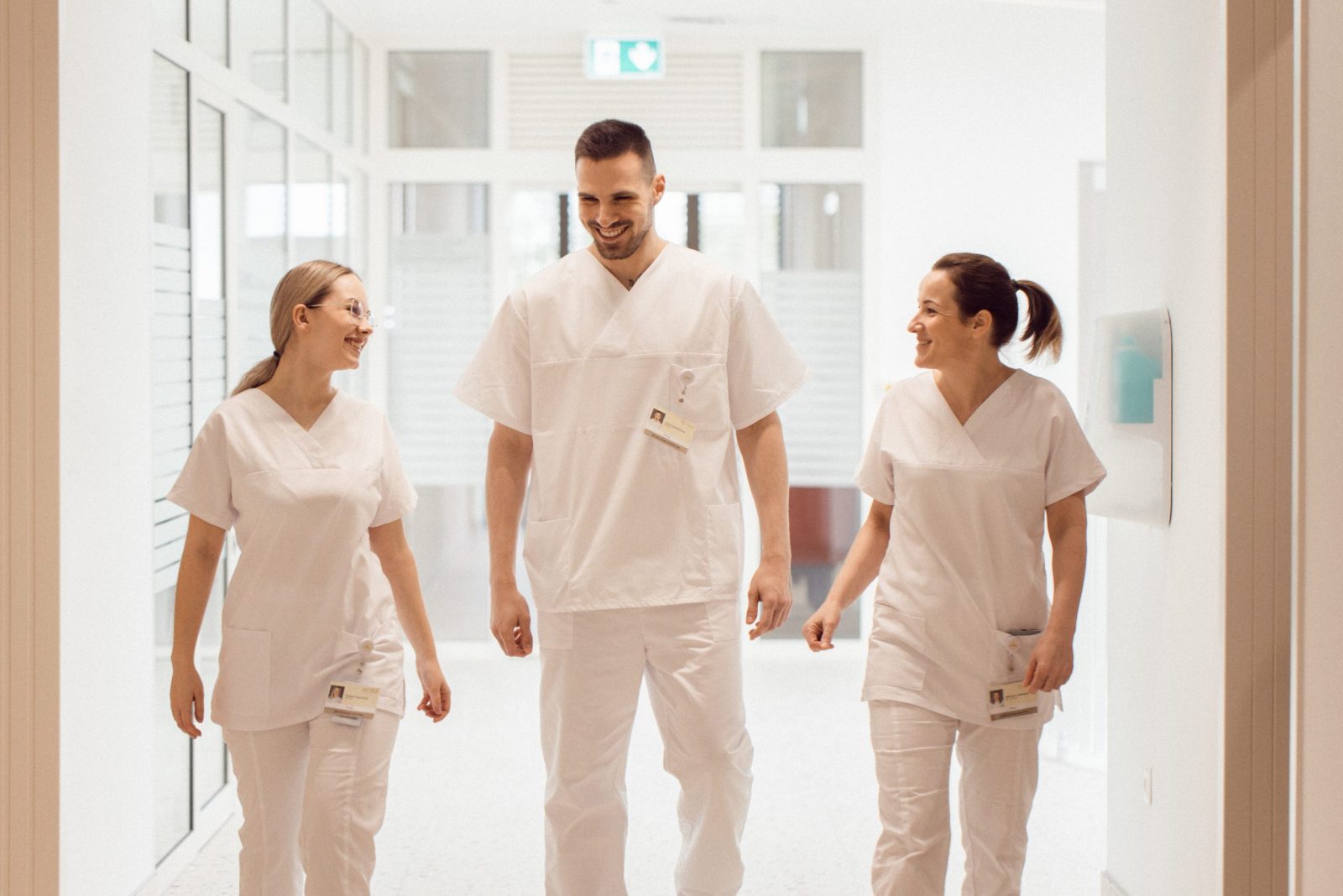 Tri medicinska radnika u bijelim uniformama hodaju hodnikom bolnice internacionalnog medicinskog centra Priora nasmijani i razgovarajući jedan s drugim.