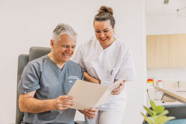 Muškarac i žena u medicinskoj odjeći nasmijani gledaju u dokument u ordinaciji.