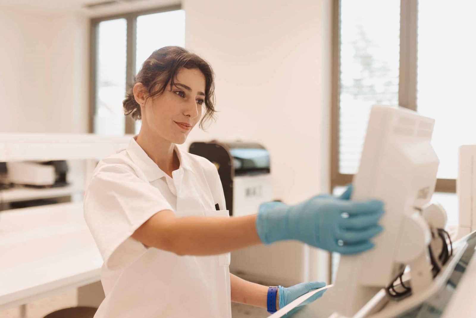 Žena u bijeloj kuti i plavim rukavicama radi na računalu u laboratoriju.