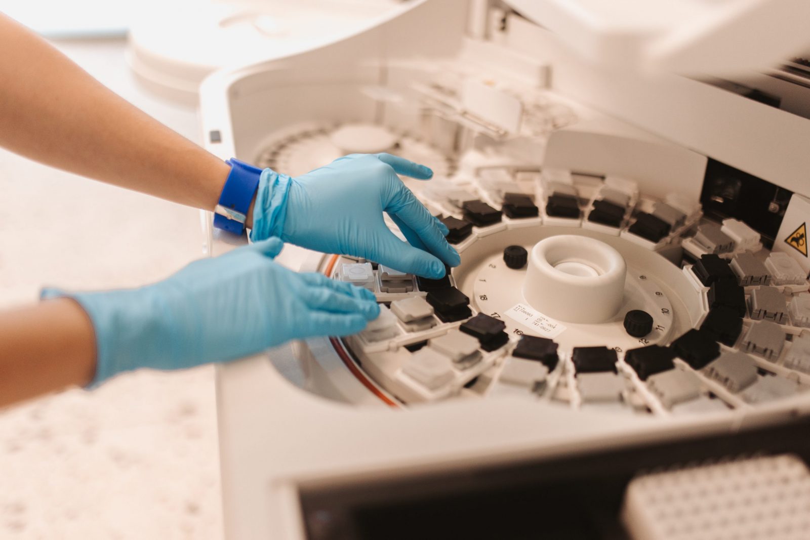 Osoba s plavim rukavicama rukuje laboratorijskim uređajem, najvjerojatnije centrifugom, unutar sterilnog okruženja.