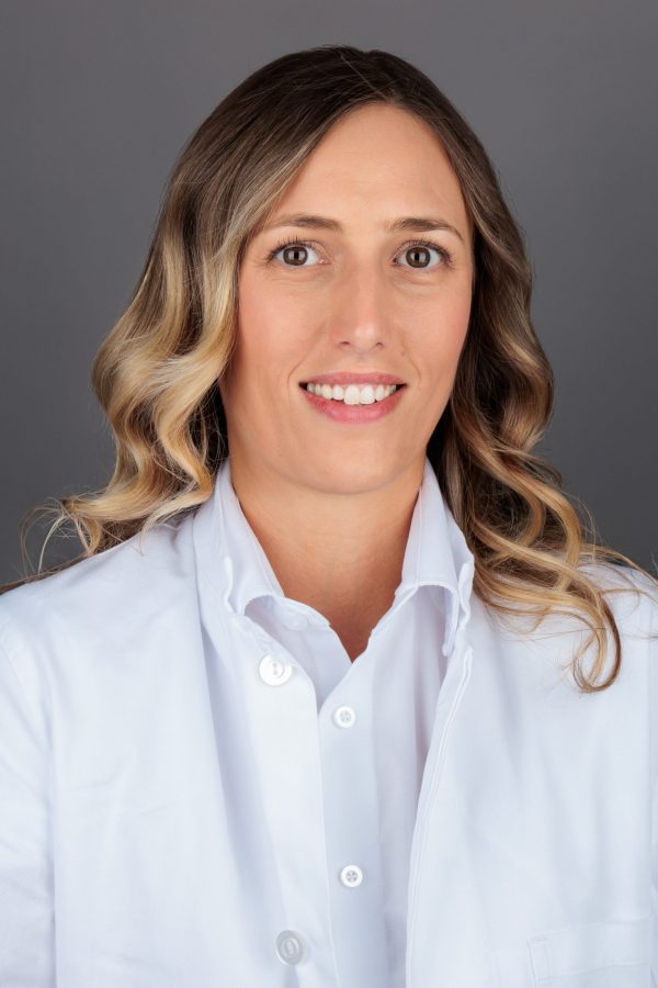 Marina Grbić Mlinarević u bijeloj košulji s kovrčavom svijetlosmeđom kosom, nasmiješena, na neutralnoj sivoj pozadini.