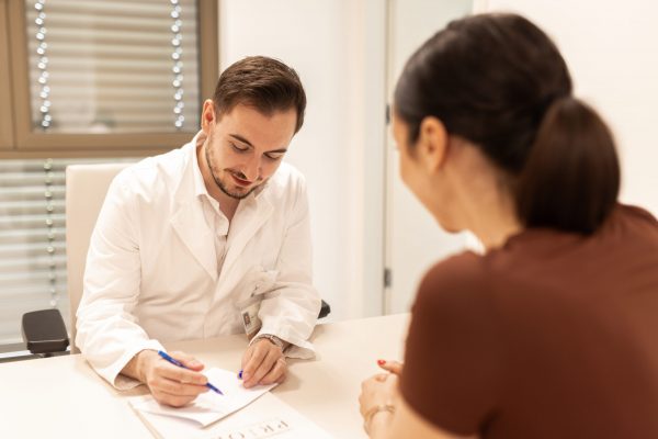 Liječnik u bijelom ogrtaču zapisuje bilješke tijekom konzultacije s pacijenticom u uredu.
