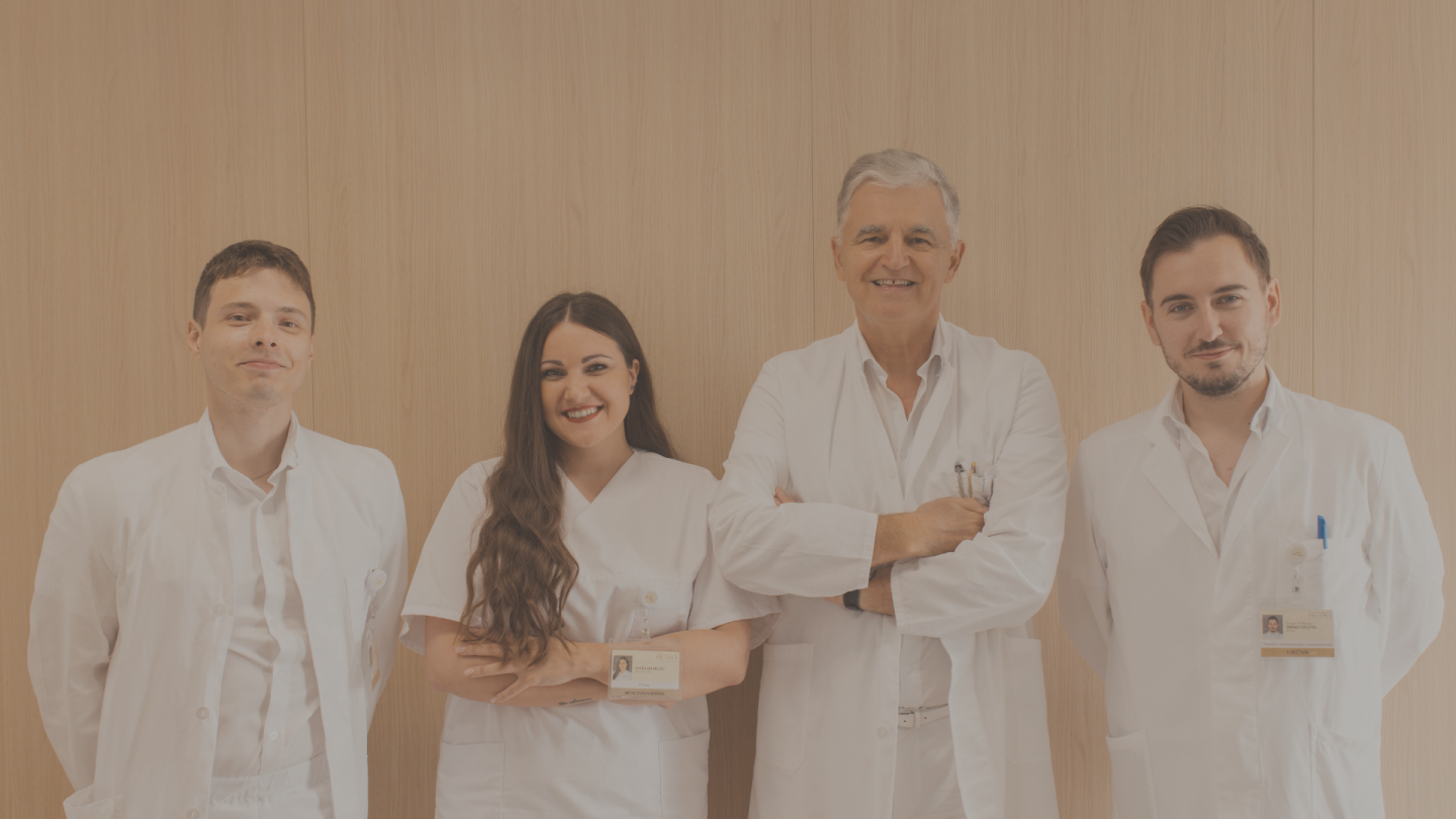 Četiri medicinska stručnjaka u bijelim kutama osmjehuju se ispred drvene pozadine.