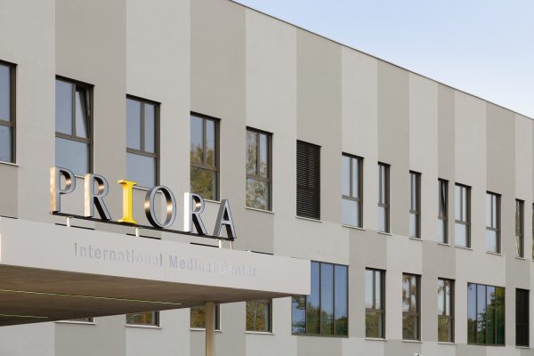 Fasada suvremene zgrade sa velikim natpisom 'PRIORA' iznad ulaza, koji pripada Međunarodnom medicinskom centru, s ravnomjernim redom prozora.