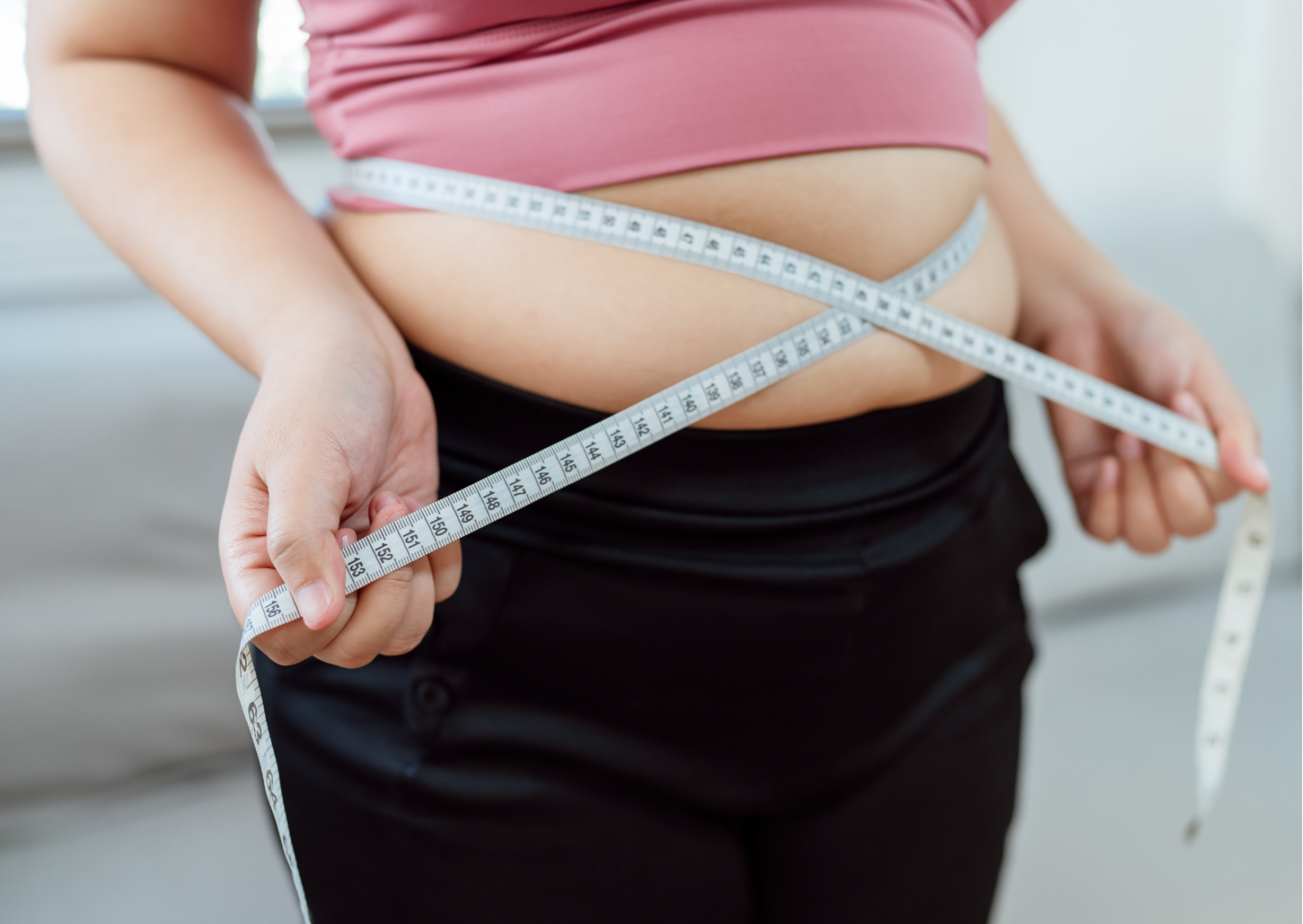 Osoba u ružičastoj majici i crnim hlačama drži metar oko struka.