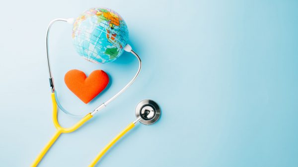 Globus, crveno srce i stetoskop na svijetloplavoj pozadini, simbolizirajući zdravstvenu zaštitu u globalnom kontekstu.