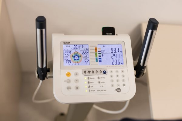 Bioimpedancijska vaga marke Tanita s dva ekrana koja prikazuju tjelesne podatke kao što su težina, postotak masnog tkiva i druge mjere, te rukohvati za mjerenje ruku.