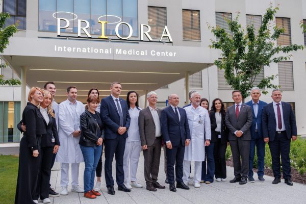 Healthcare staff and executives pose for a group photo beneath the “PRIORA International Medical Center” sign at a modern clinic entrance.