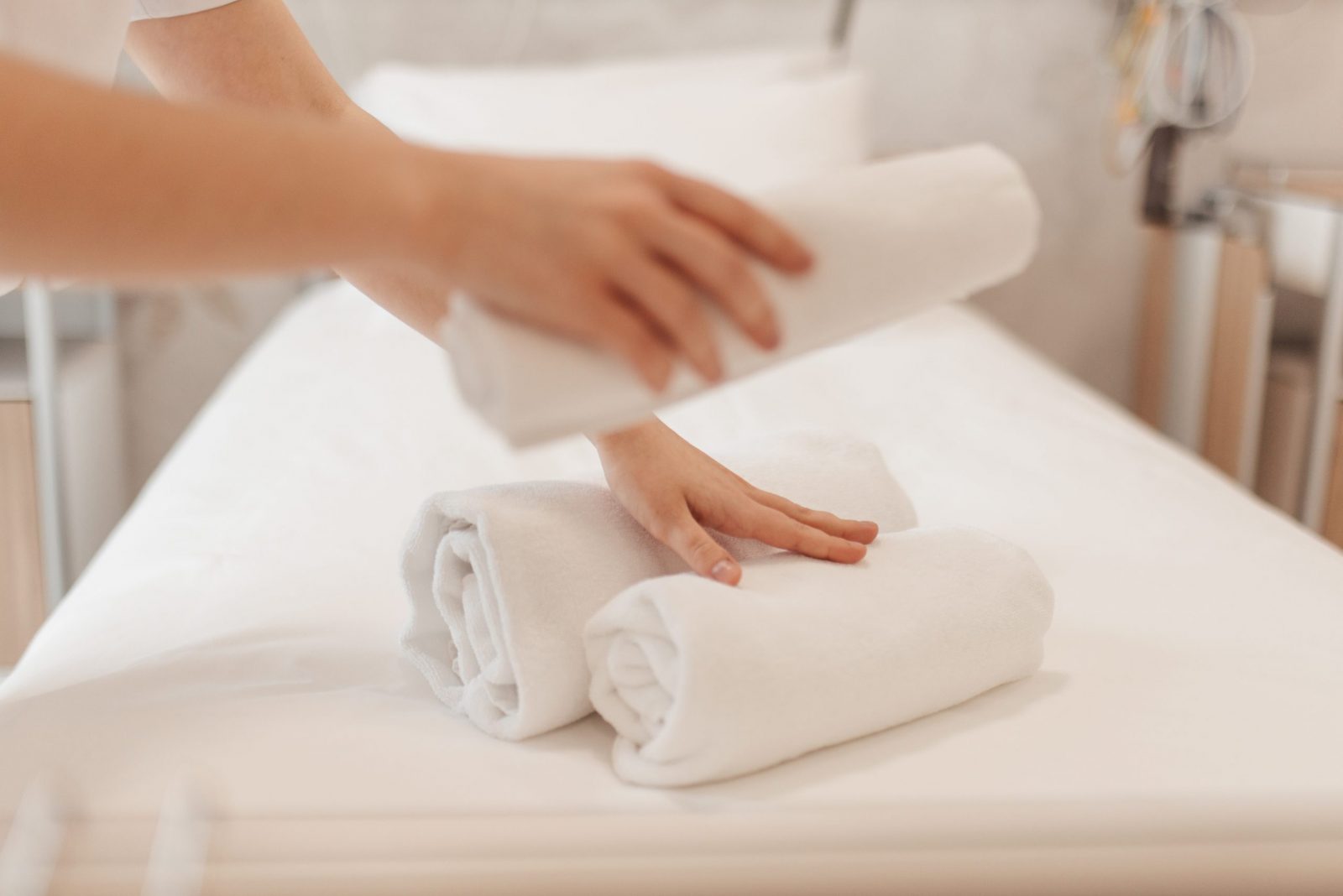Hands arranging three rolled white towels on a clean massage table.