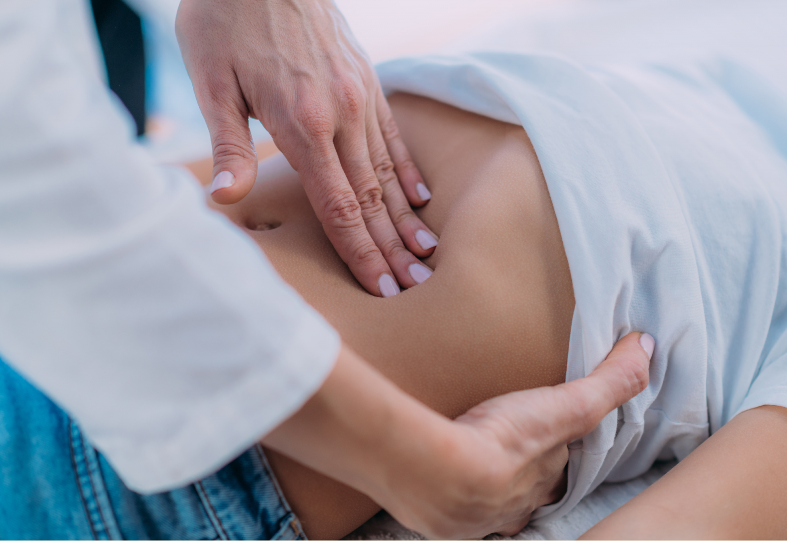 Close-up of a practitioner’s hands performing abdominal palpation or massage on a person’s exposed stomach.