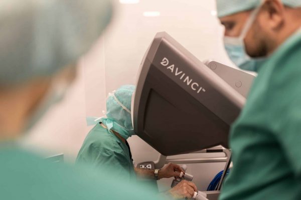 Kirurg upravlja robotskim sustavom Da Vinci tijekom operacije, noseći zelenu kiruršku odjeću i zaštitnu opremu.