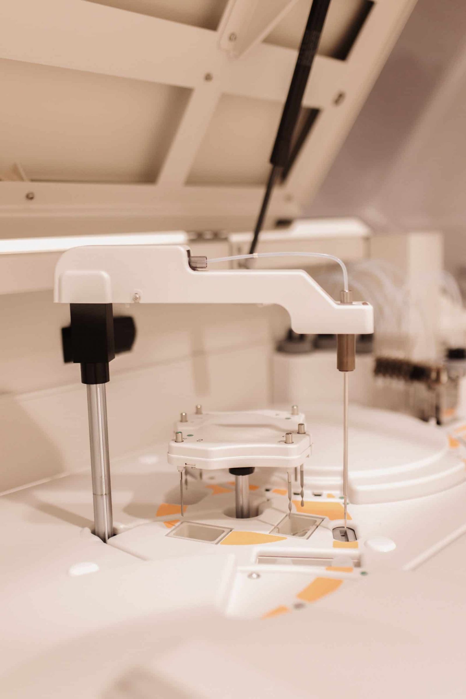 Laboratorijska oprema bijele boje s pokretnim dijelovima i mehaničkim rukama unutar postrojenja, vjerojatno za analizu uzoraka.