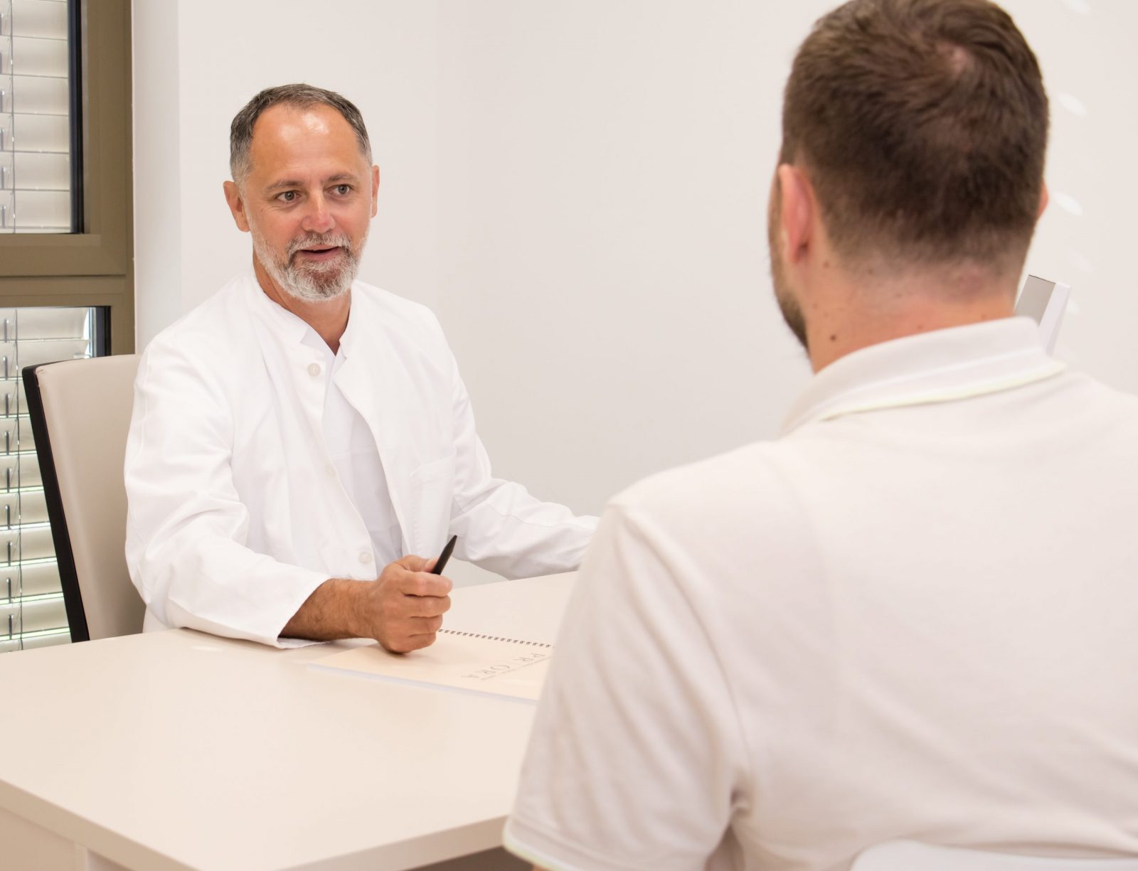 Liječnik u bijelom mantilu razgovara s pacijentom u ordinaciji.