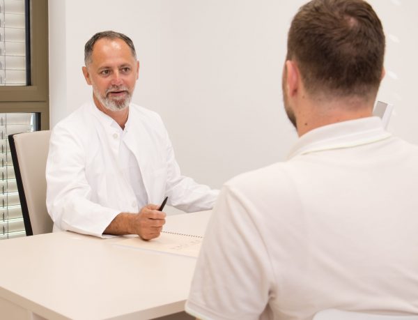 Liječnik u bijelom mantilu razgovara s pacijentom u ordinaciji.