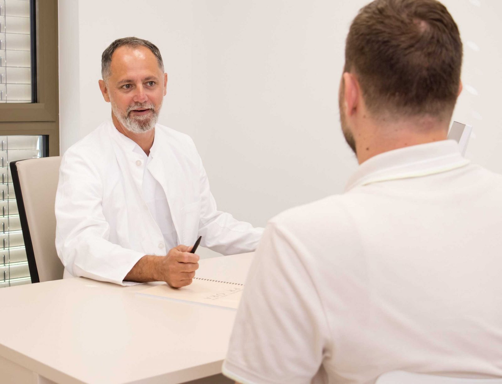 Liječnik u bijelom mantilu razgovara s pacijentom u ordinaciji.