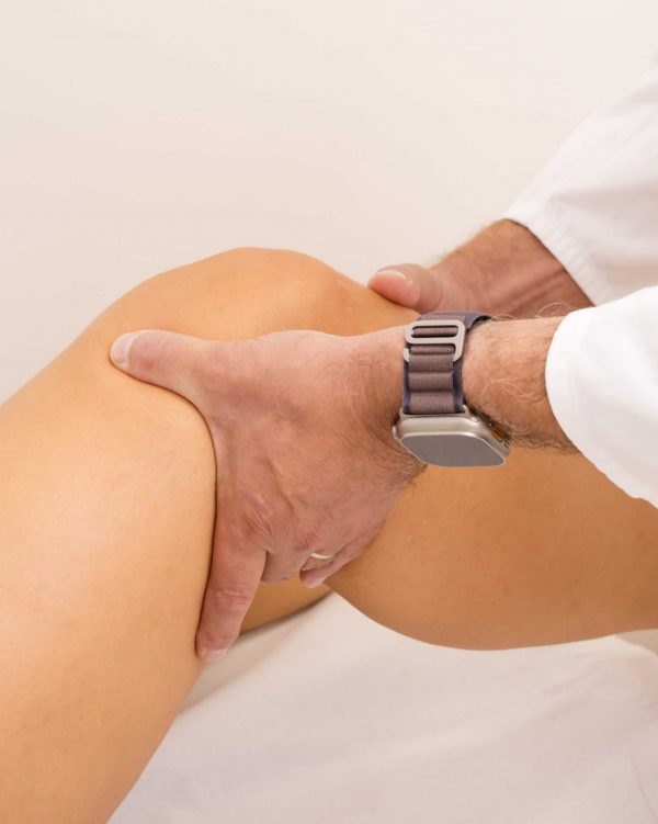 Osoba u bijelom rukavu pregledava koljeno druge osobe, noseći pametni sat.