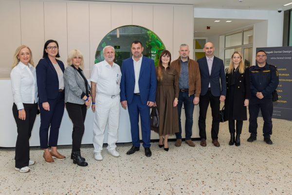 Skupina od deset ljudi u poslovnoj, medicinskoj i službenoj odjeći pozira u predvorju moderne stomatološke klinike, ispred okruglog staklenog prozora i pulta, s informacijskom pločom „Adria Dental Group” desno.