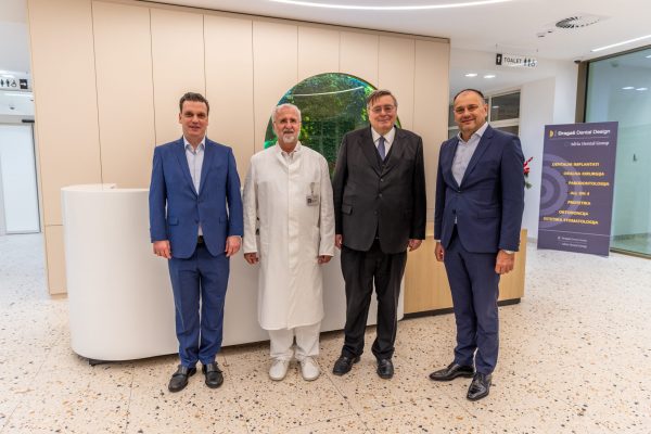 Četvorica muškaraca—trojica u odijelima i jedan u bijeloj liječničkoj kuti—poziraju ispred recepcije u modernoj stomatološkoj ordinaciji, s natpisom „Dragaš Dental Design” i popisom usluga u pozadini.