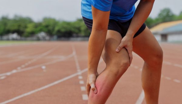 Person on a running track clutching their calf and thigh, with a reddened lower leg indicating pain.