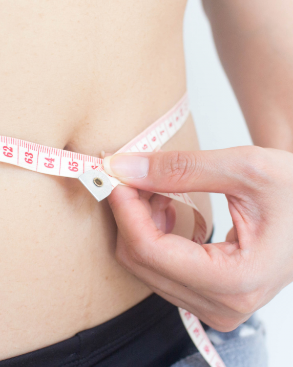 Krupni plan ruke koja mjernom trakom mjeri opseg struka.