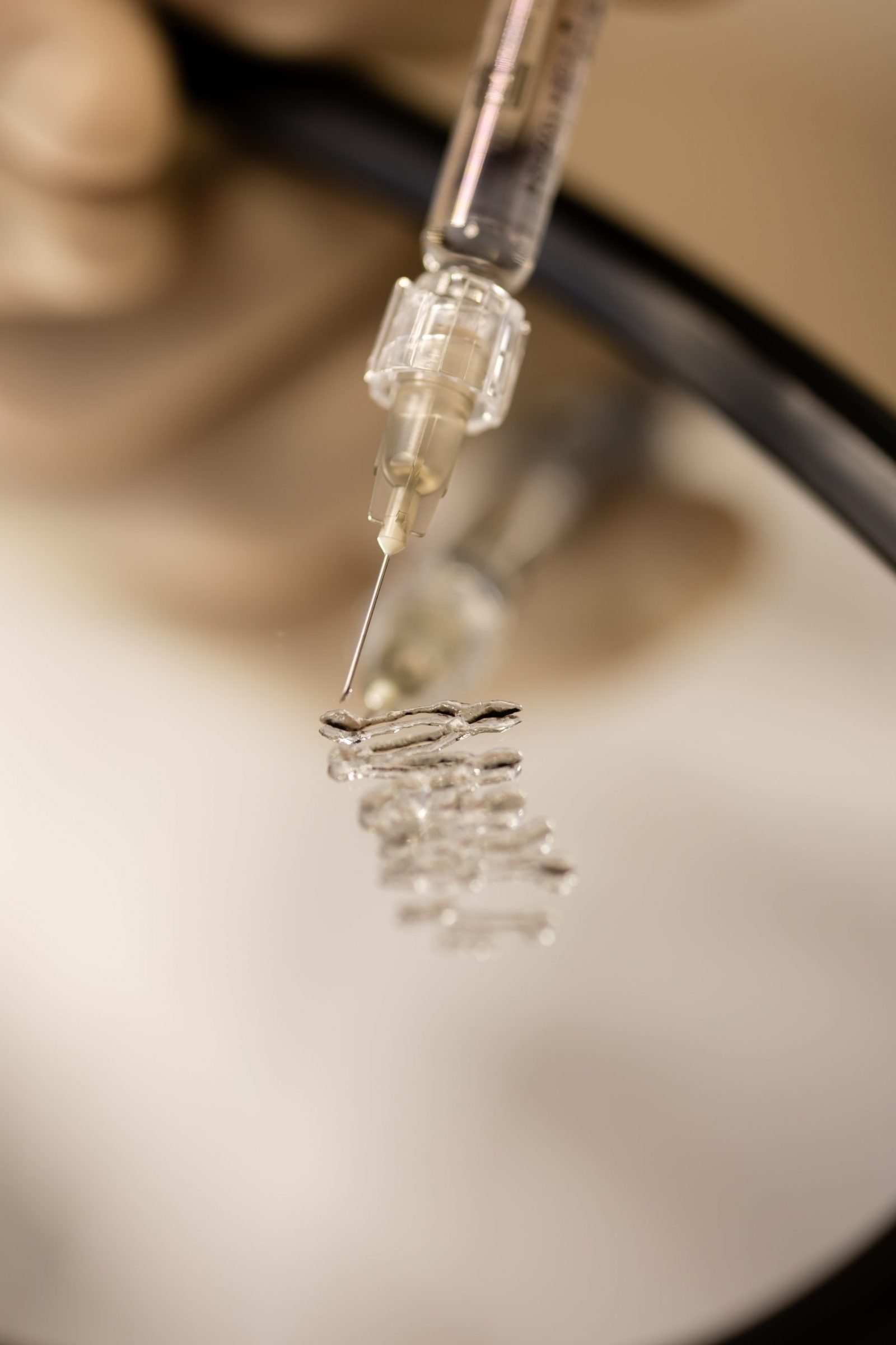 Makro snimka igle štrcaljke koja nanosi kap tekućine na mali metalni mrežasti cilindar.