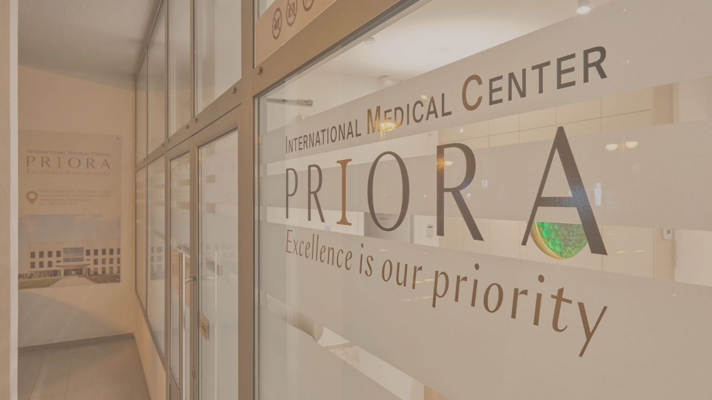 Glass entrance of International Medical Center PRIORA with the motto 'Excellence is our priority' and reception inside.